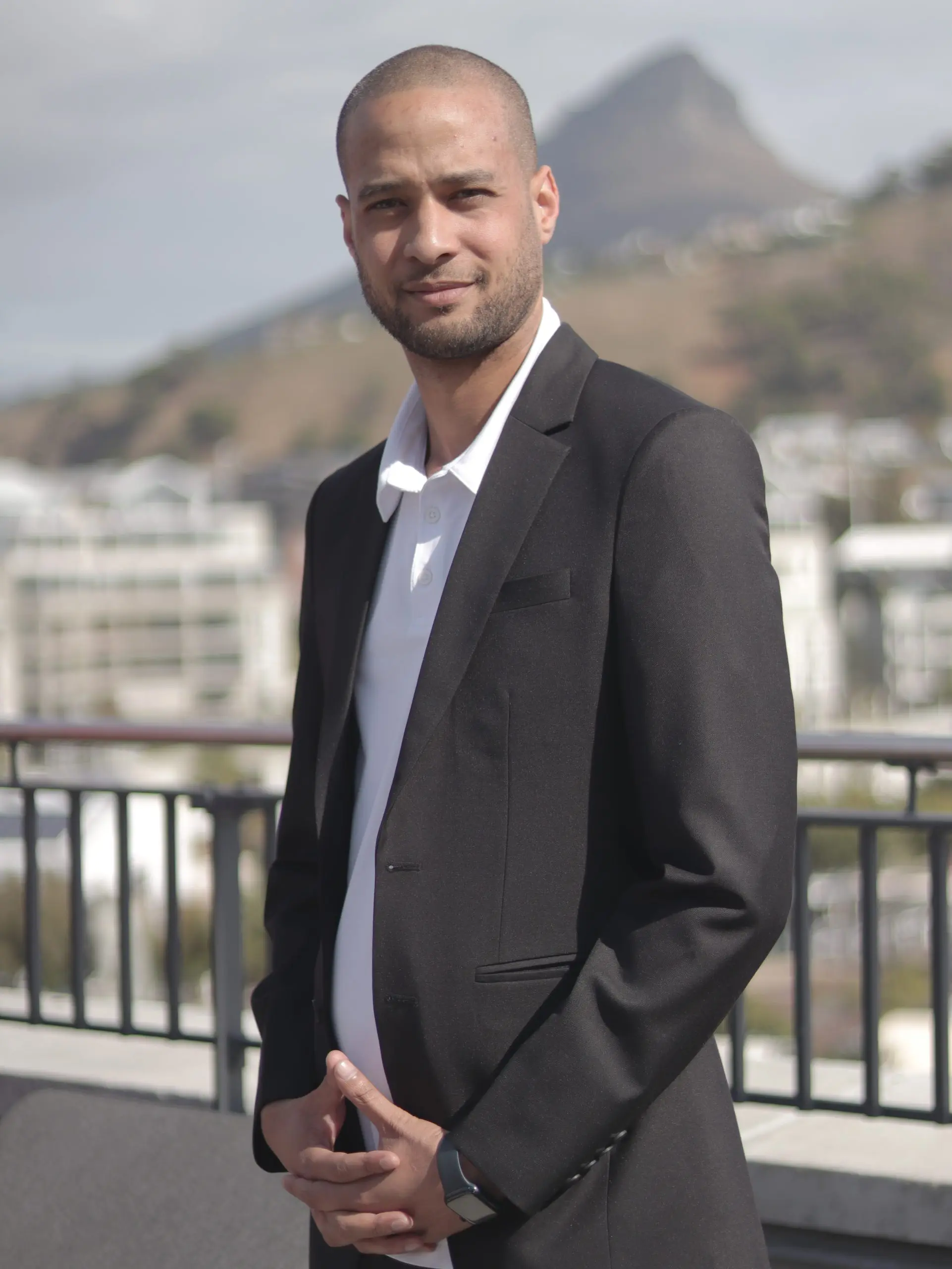 Asheeq Adams in a dark suit on a Cape Town rooftop with Lion's Head behind