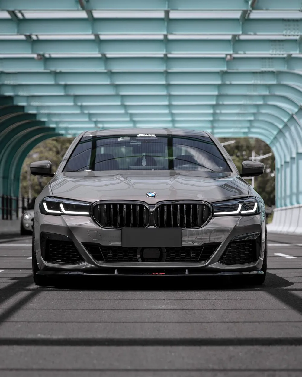 A grey BMW 5 Series saloon, nose-on, in a glass-roofed tunnel