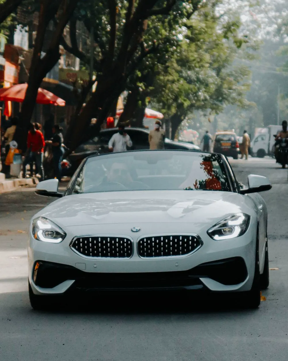 A white BMW Z4 roadster with the roof down on a tree-lined city street