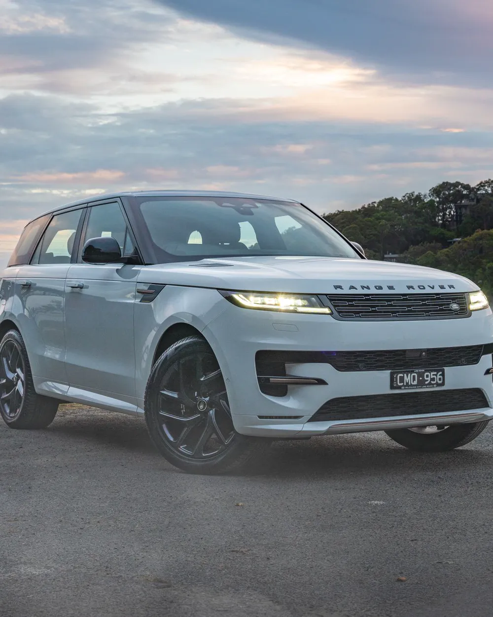 A white Range Rover Sport parked by the water at sunrise, mist rising off the bay