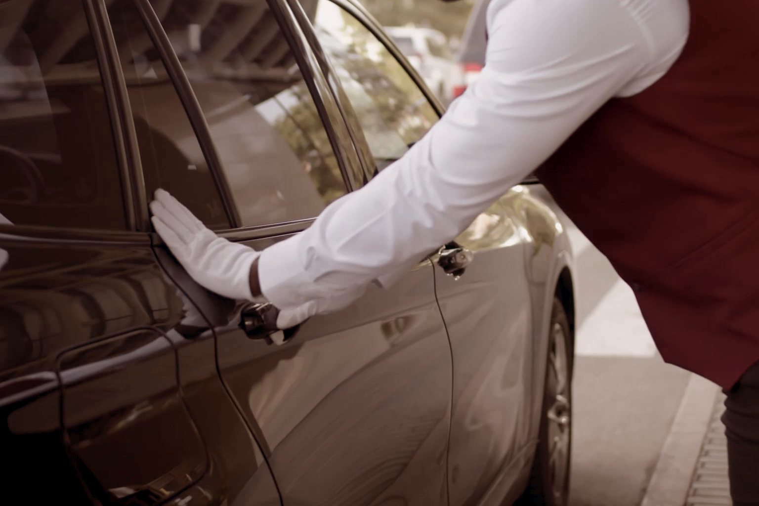 A white-gloved Luxury Lane chauffeur opening the rear door of a Mercedes-Benz