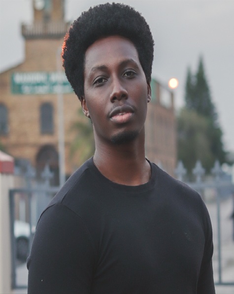 Twaha standing in front of a dark brick wall